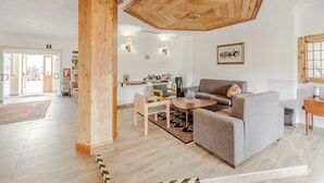 A spacious living room with a high wooden ceiling, a grey sofa, a wooden coffee table, and a wooden sideboard. - Hotiday Bormio Valdidentro (San Carlo)