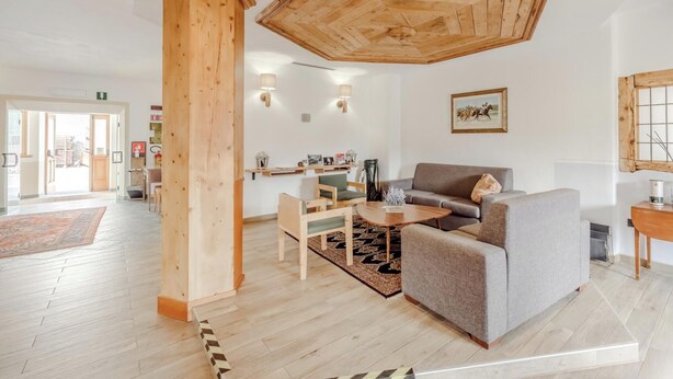 A spacious living room with a high wooden ceiling, a grey sofa, a wooden coffee table, and a wooden sideboard. - Hotiday Bormio Valdidentro (San Carlo)
