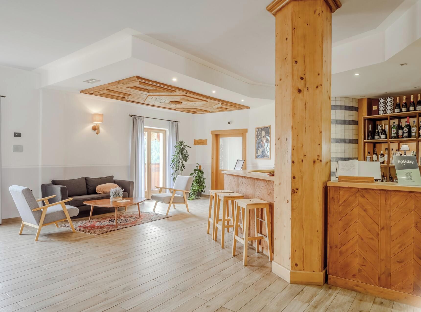 Een moderne hotellobby met een houten receptiebalie, een bar, een zithoek en een groot raam met gordijnen.