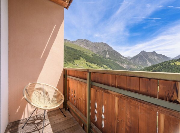 A balcony with a wicker chair, wooden railing, and a mountain view. - Hotiday Bormio Valdidentro (San Carlo)