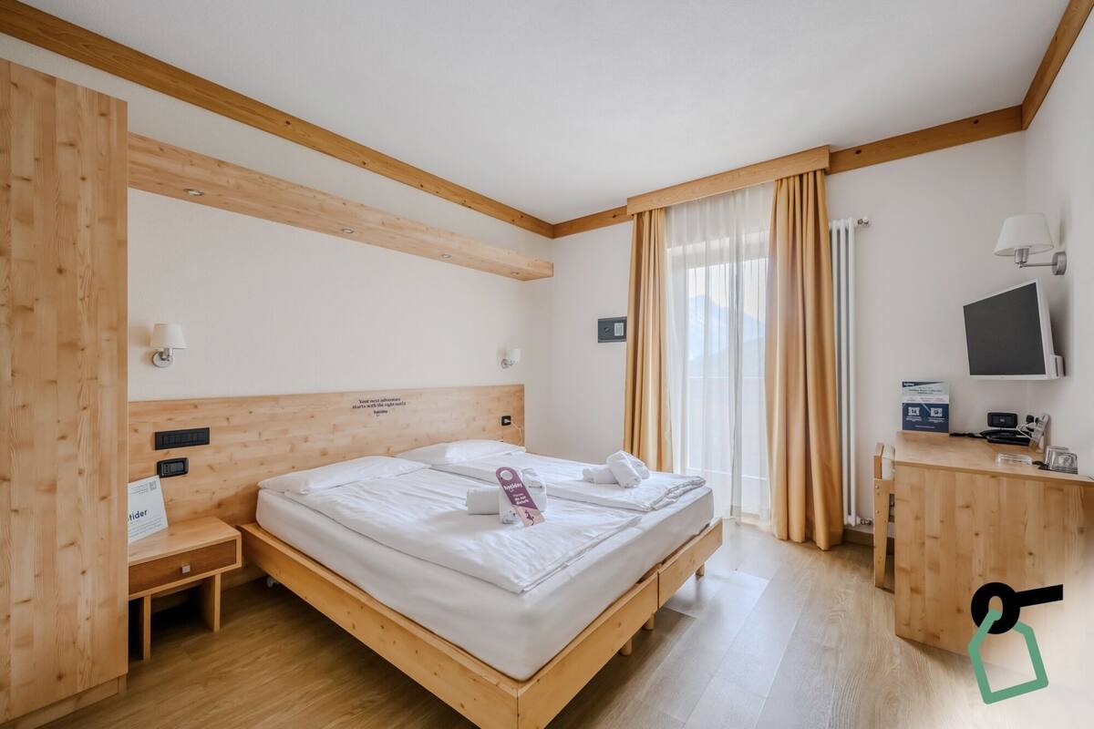 Una camera d'albergo con un letto di legno, un comodino, una lampada e una scrivania con computer e telefono.