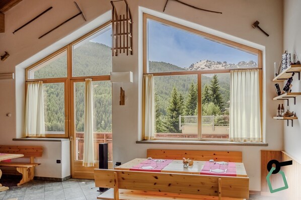 Una stanza con ampie finestre che offrono vista sulle montagne, una panca di legno e un tavolo apparecchiato per la cena.