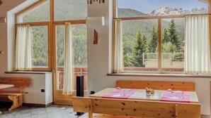 A room with large windows offering mountain views, a wooden bench, and a table set for dining. - Hotiday Bormio Valdidentro (San Carlo)