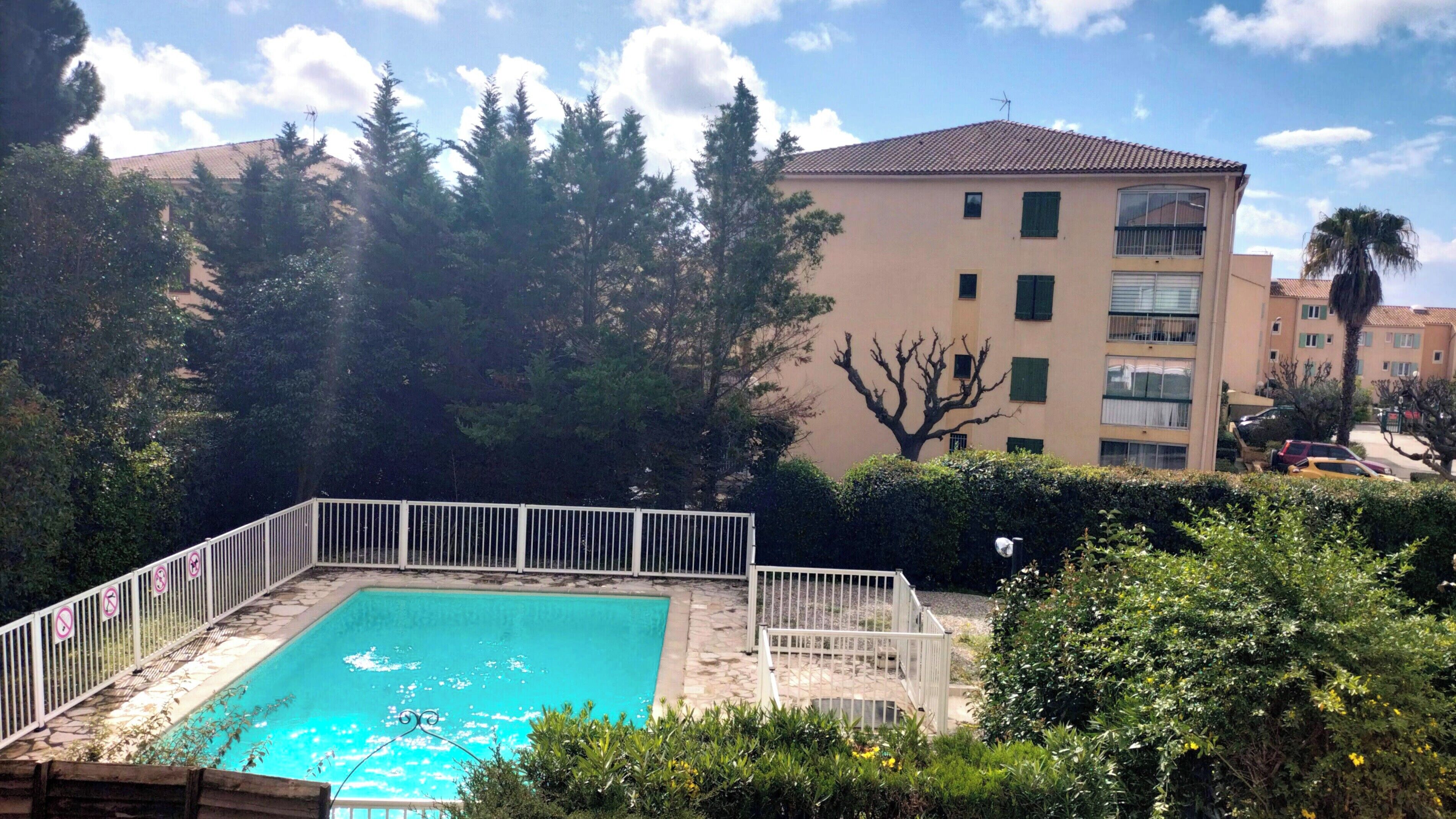 A swimming pool surrounded by a white fence, with a building in the background.