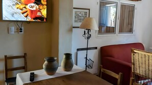 En stue med fjernsyn, et bord med fjernbetjening, to vaser, en lampe og en rød sofa.