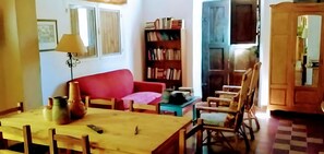 Una sala de estar acogedora con un sofá rojo, una mesa de madera con un florero, una estantería y una puerta azul.