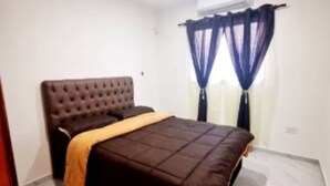 Ein Schlafzimmer mit einer gesteppten Kopfteil, einem Bett mit dunkler Bettdecke und einer gelben Tagesdecke.