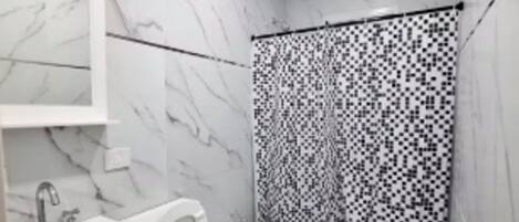 A modern bathroom with a marble floor, a white vanity with a mirror, a toilet, and a shower area with a patterned curtain.