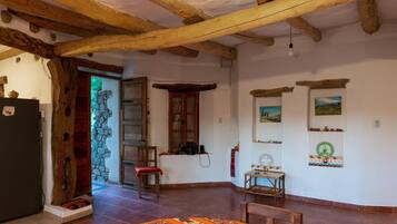 A rustic room with exposed wooden beams, a stone wall, a wooden door, a red chair, a small table, and a patterned rug.