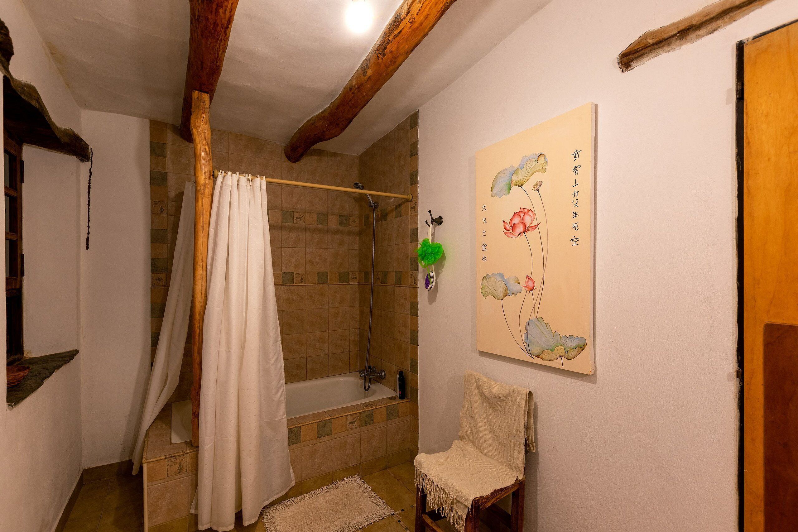 Een badkamer met een badkuip, douche, houten balken, een handdoekhouder en een schilderij aan de muur.