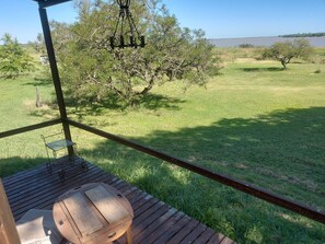 Eine Holzterrasse mit einem rustikalen Fass, einer hängenden Leuchte und Blick auf ein grasbewachsenes Feld mit Bäumen.