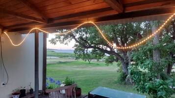 Un patio al aire libre con luces colgantes, un banco de madera y plantas en macetas.