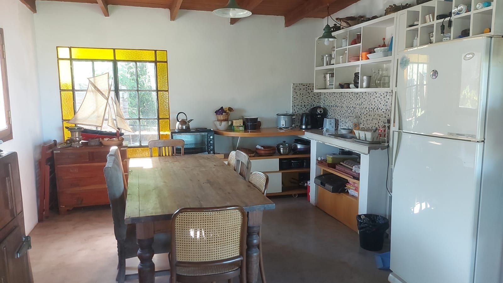 Una cocina con una mesa de madera, sillas, un refrigerador y diferentes electrodomésticos.