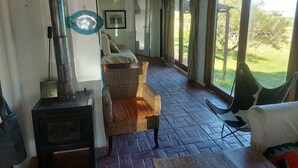 Ein Zimmer mit Kamin, Korbmöbeln und großen Fenstern mit Blick ins Freie.