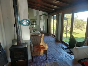 Una habitación con chimenea, mobiliario de mimbre y ventanas amplias que dan al exterior.