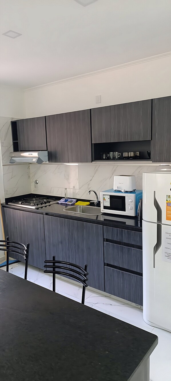 A modern kitchen with grey cabinets, a black countertop, a white refrigerator, and a microwave.