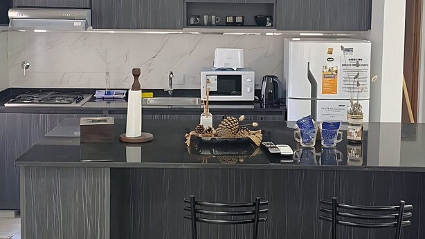Une cuisine moderne avec des meubles de couleur sombre, un îlot central doté de tabourets de bar et un four encastré.
