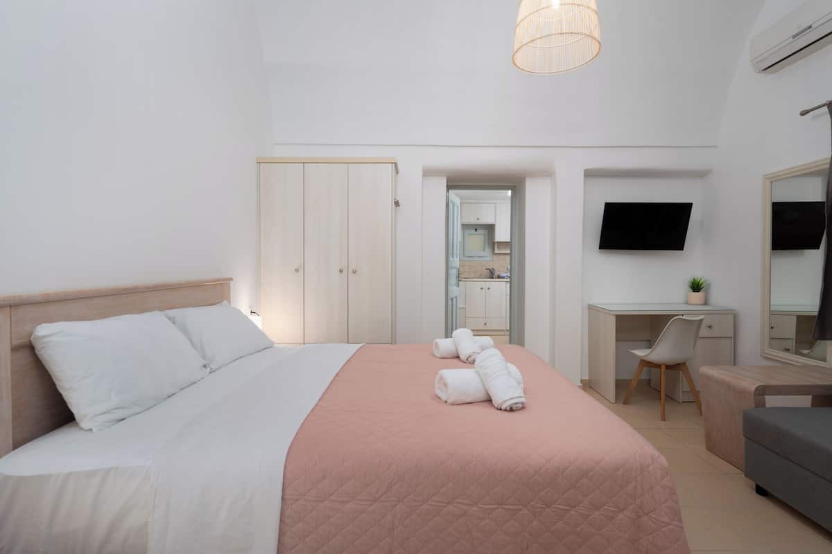 Quarto de hotel com cama, escrivaninha, cadeira, televisão e guarda-roupa.