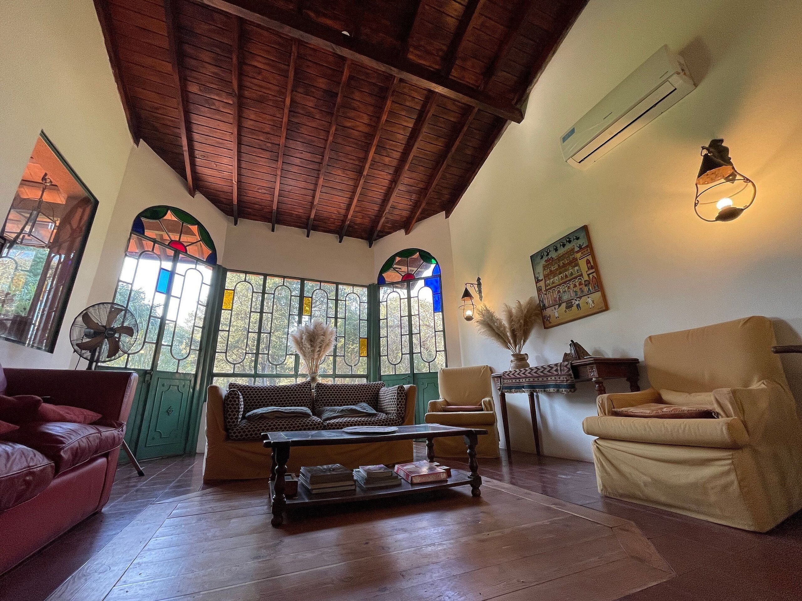 Una sala de estar acogedora con techo de madera, una puerta verde, un sofá, una silla y un ventilador.