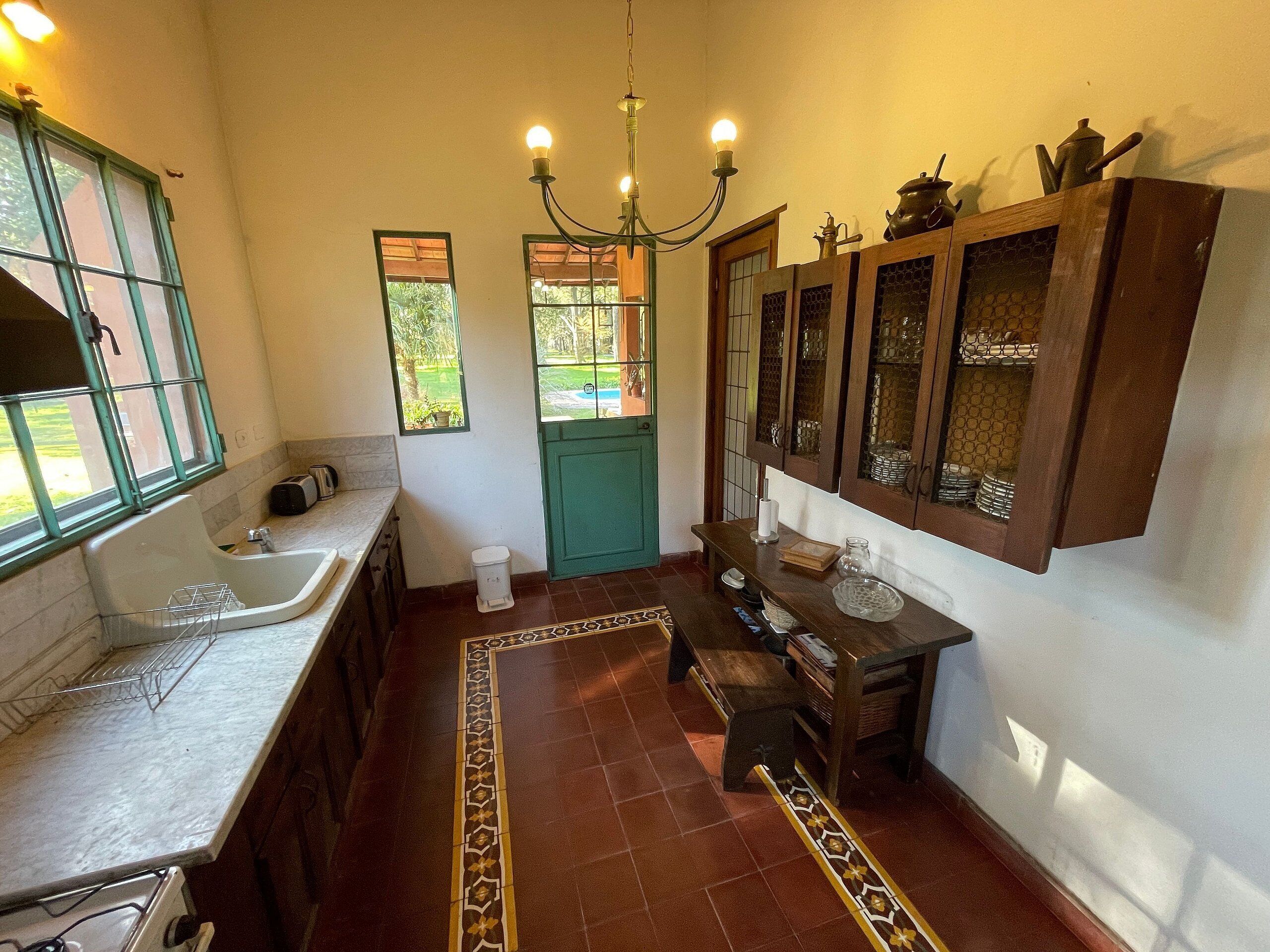 A kitchen with a sink, stove, and a chandelier. There are windows and a door leading outside.