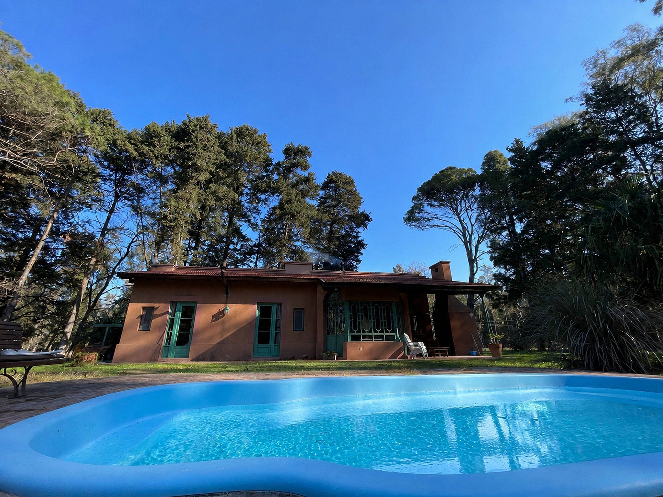 A house with a swimming pool, surrounded by trees and a clear sky.