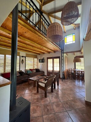Amplia sala de estar con escalera de madera, una mesa de comedor con sillas y una chimenea.