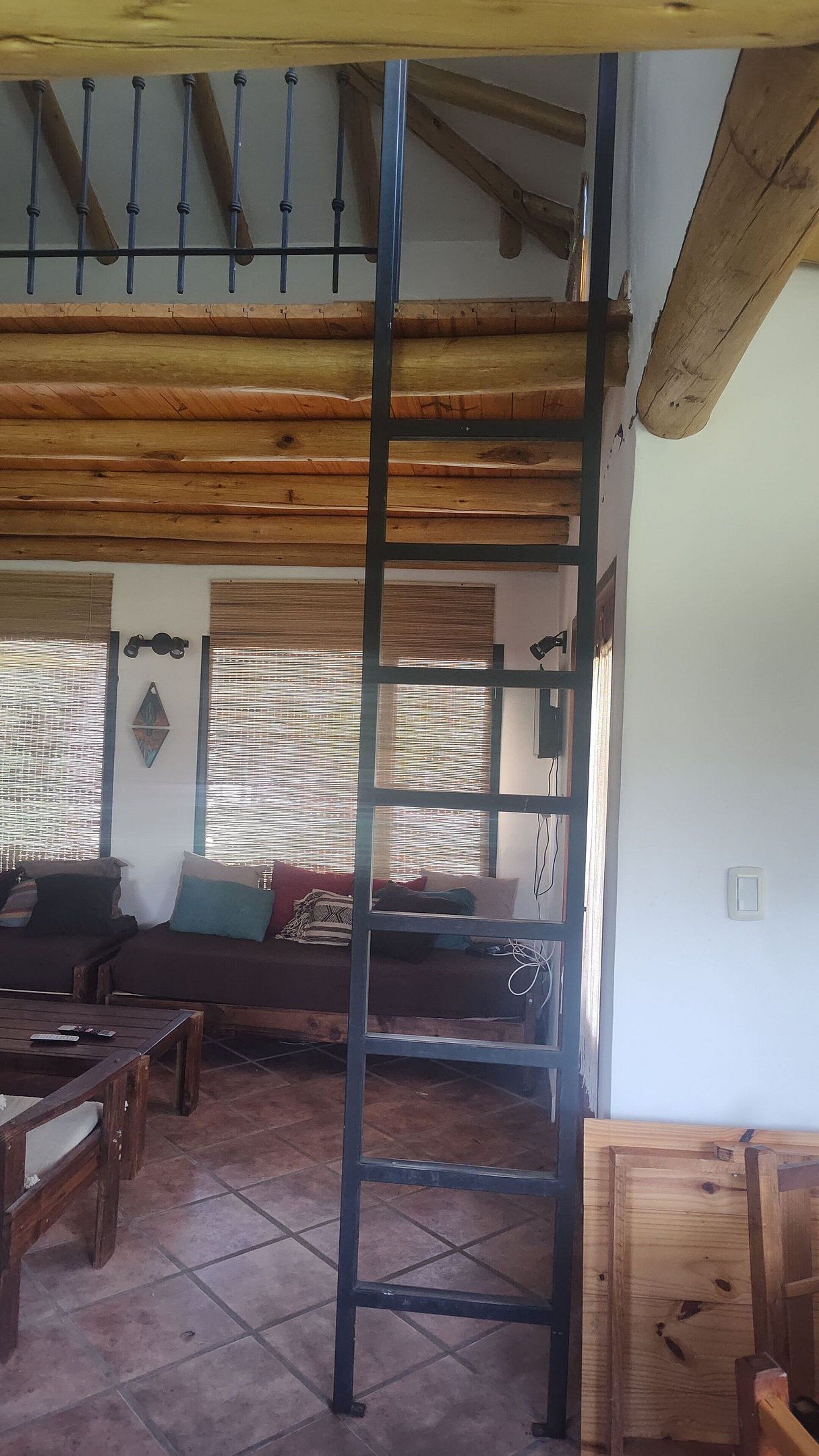 Ein Zimmer mit Holzbalkendecke, einer Sofagarnitur, einem Couchtisch und einer Leitern.