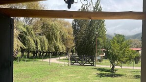 A covered patio area with a tiled floor, a hanging chandelier, and a view of a grassy landscape with trees and a distant mountain range.