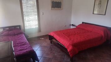 Ein Schlafzimmer mit zwei Betten, eines mit roter Bettdecke und das andere mit violetter Bettdecke.