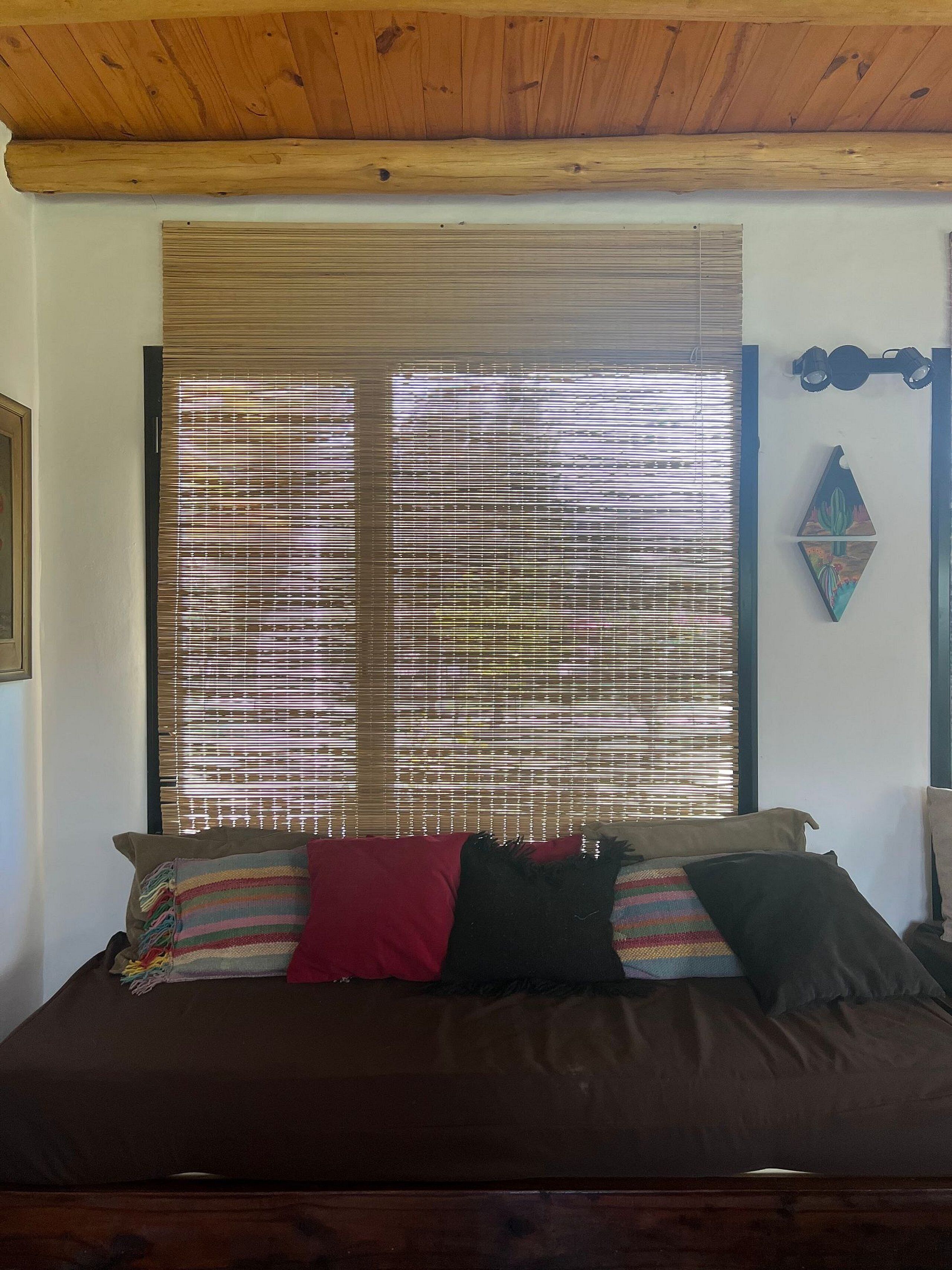 Une chambre avec une grande fenêtre recouverte de stores, un lit avec de nombreux oreillers et un plafond en bois.