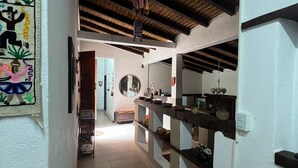 A narrow hallway with a tiled floor, a wooden ceiling, and a kitchen area with shelves and a hanging pot.