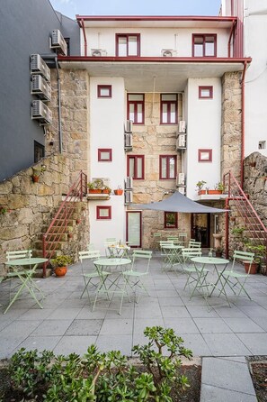 A building with a stone facade, multiple windows, and a patio area with outdoor seating. - GuestReady - Invicta Porto GuestHouse - Flat 202 (Porto)