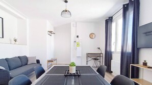 Una sala de estar moderna con un sofá, una mesa de comedor con una planta, un escritorio y un amplio ventanal con cortinas.