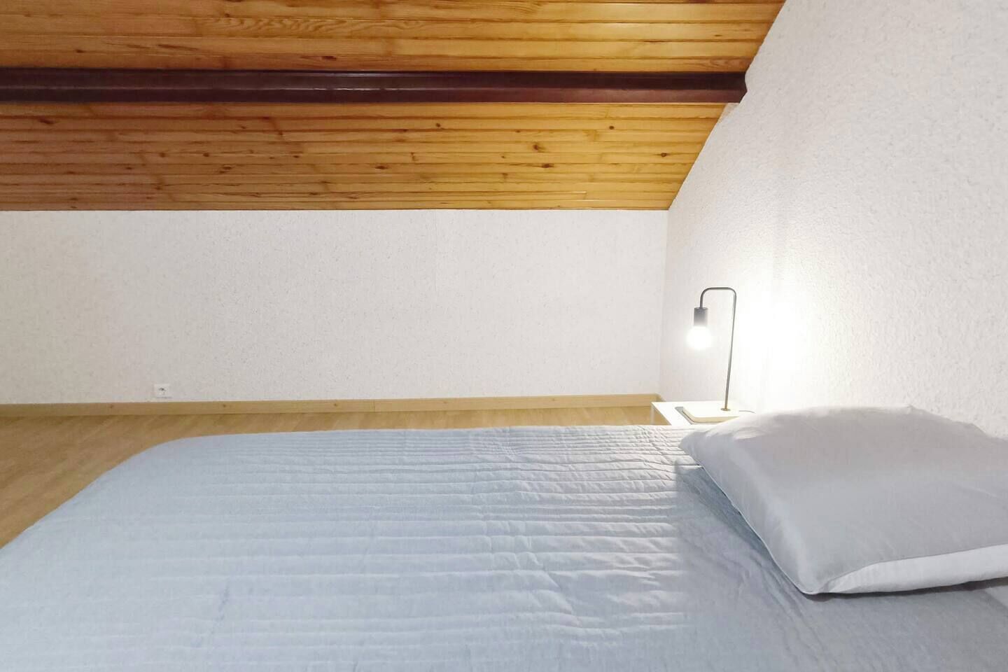 Une chambre avec un plafond en bois, un lit avec une literie blanche et une lampe de chevet.