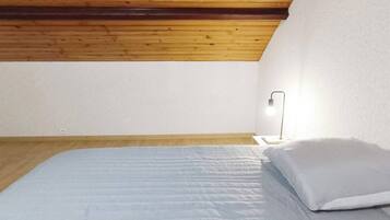 Une chambre avec un plafond en bois, un lit avec une literie blanche et une lampe de chevet.