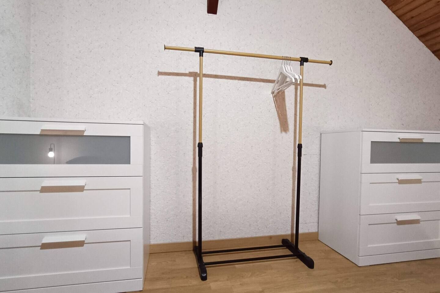 Une pièce avec deux commodes blanches, un plancher en bois et un plafond au design incliné.