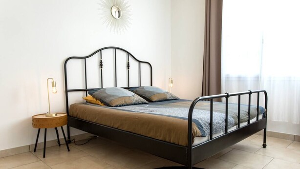 Una cama individual con estructura metálica negra, una mesita de noche redonda de madera y una alfombra redonda en el suelo.