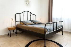 Una cama individual con estructura metálica negra, una mesita de noche redonda de madera y una alfombra redonda en el suelo.