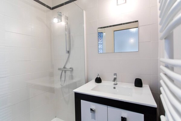 Un baño moderno con ducha de vidrio, un lavamanos blanco y dos dispensadores de jabón negros, y un espejo sobre el lavamanos.