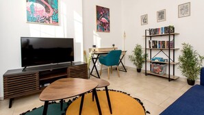 Una sala de estar con televisor, muebles de madera, estantería y plantas decorativas.
