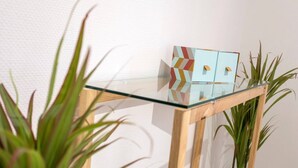 Una mesa con superficie de vidrio y una caja con diseño geométrico encima, flanqueada por dos macetas.