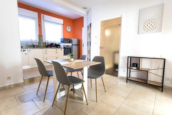 Una cocina moderna con armarios blancos, una mesa de comedor con cuatro sillas y una mesita auxiliar con una planta.