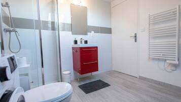 Une salle de bain moderne avec une douche à parois de verre, des toilettes blanches, un meuble-lavabo rouge avec des tiroirs et un porte-serviettes.