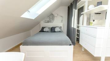 Une chambre moderne avec un plafond en pente, un lit avec une literie grise, une commode blanche et un puits de lumière.