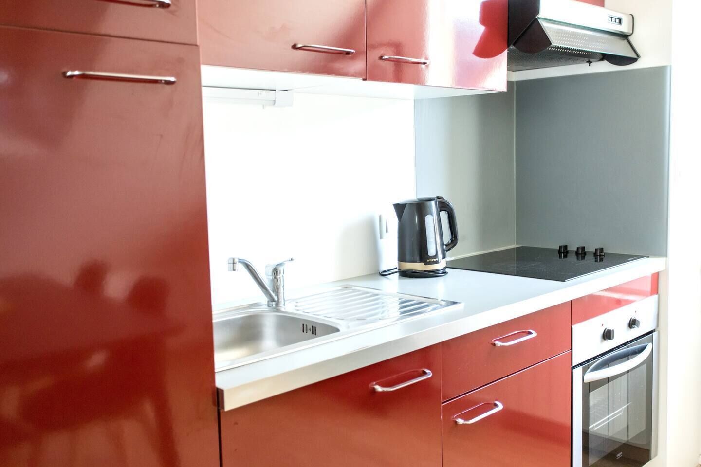 Une cuisine avec des meubles de rangement rouges, un évier en acier inoxydable, une bouilloire et une cuisinière.
