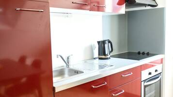 Une cuisine avec des meubles de rangement rouges, un évier en acier inoxydable, une bouilloire et une cuisinière.