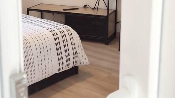 A hotel room with a bed, a TV mounted on the wall, a desk with a lamp, and a door with a handle. - Studio Le Brivet City Center ☆ Parking ☆ Terrace (Pontchâteau)