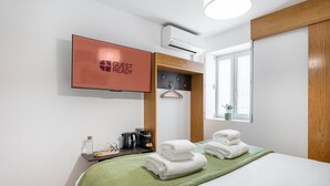 A hotel room with a bed, a TV mounted on the wall, a coffee maker, and a window with a plant. - GuestReady - Invicta Porto GuestHouse - Room 001 (Porto)