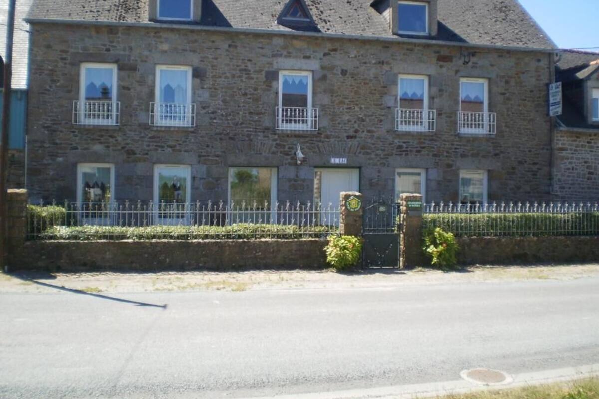 Un bâtiment en pierre doté de nombreuses fenêtres et de balcons, une entrée fermée par un portail et une route pavée devant.