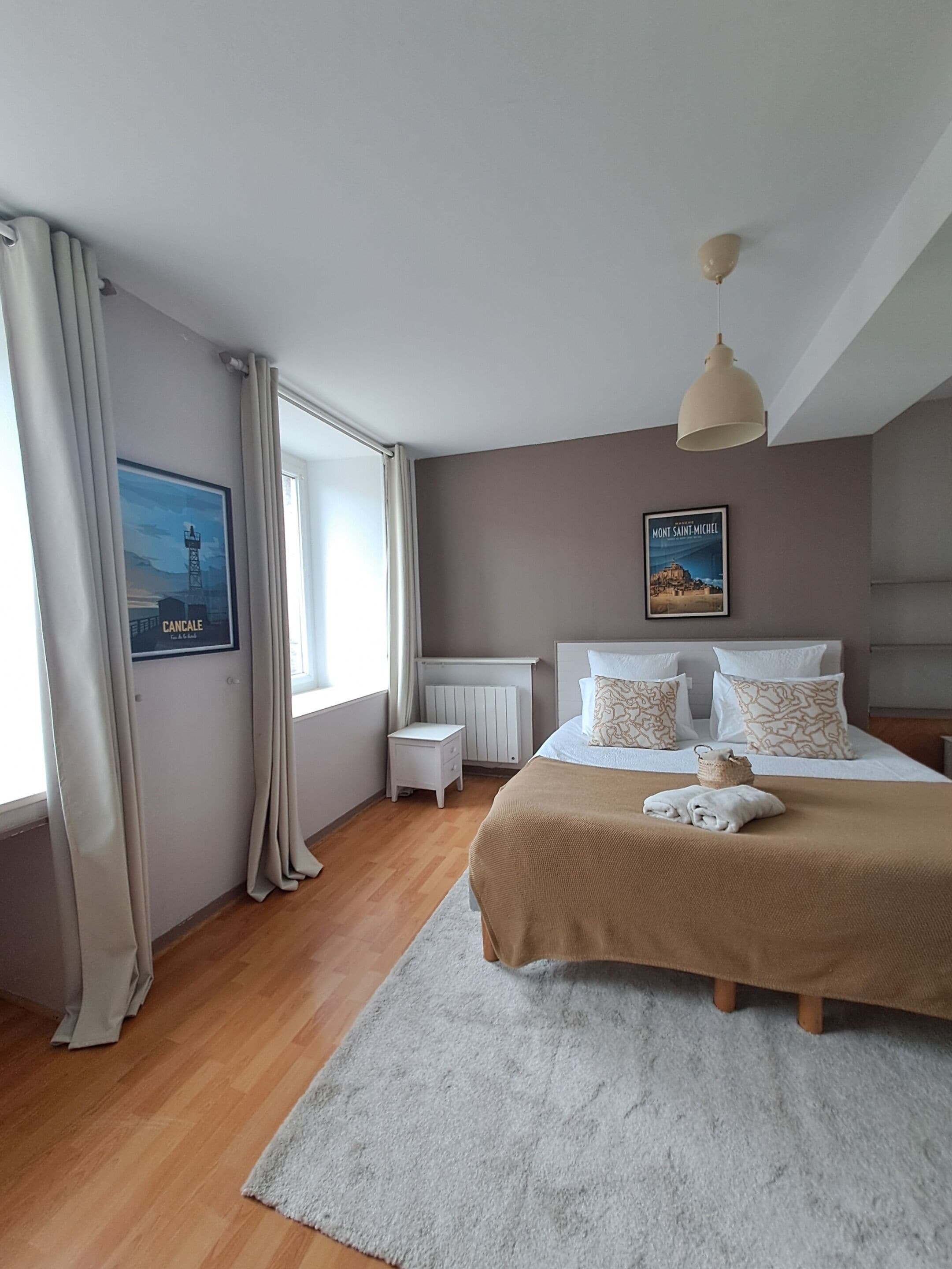 Une chambre à coucher avec un lit, une table de chevet, un radiateur, une fenêtre avec des rideaux et une affiche accrochée au mur.